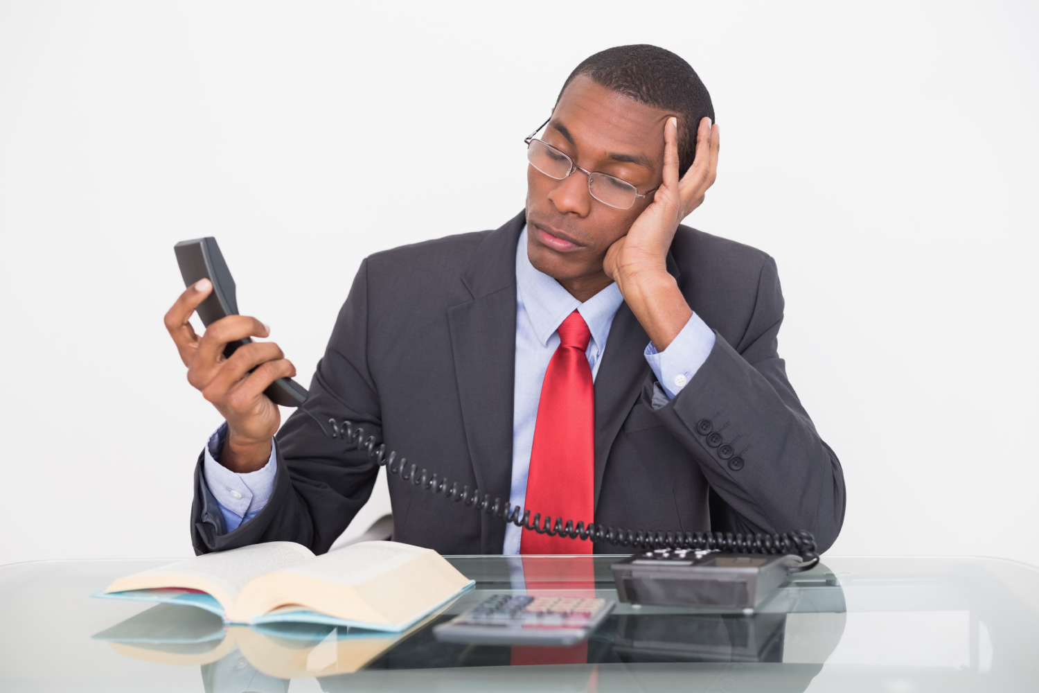 Young tensed young Afro businessman looking at telephone receiver against white background<br />
