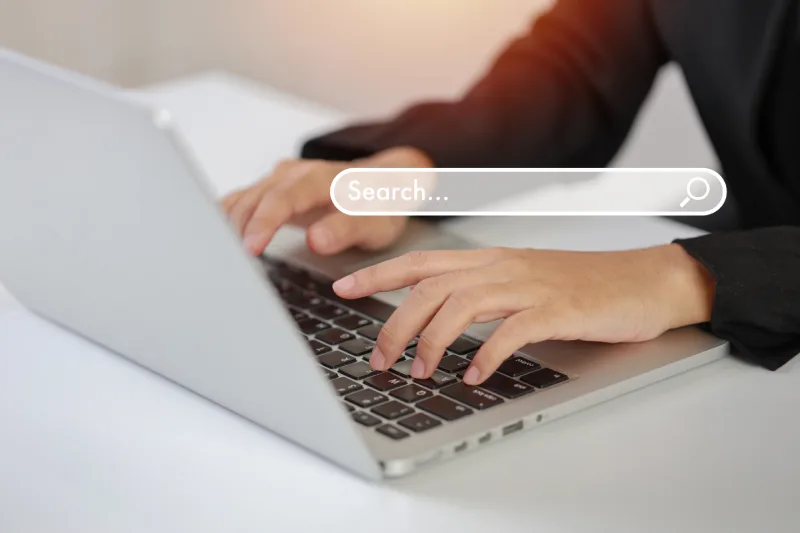 A person typing on a silver laptop with a digital search bar graphic floating over the keyboard area.