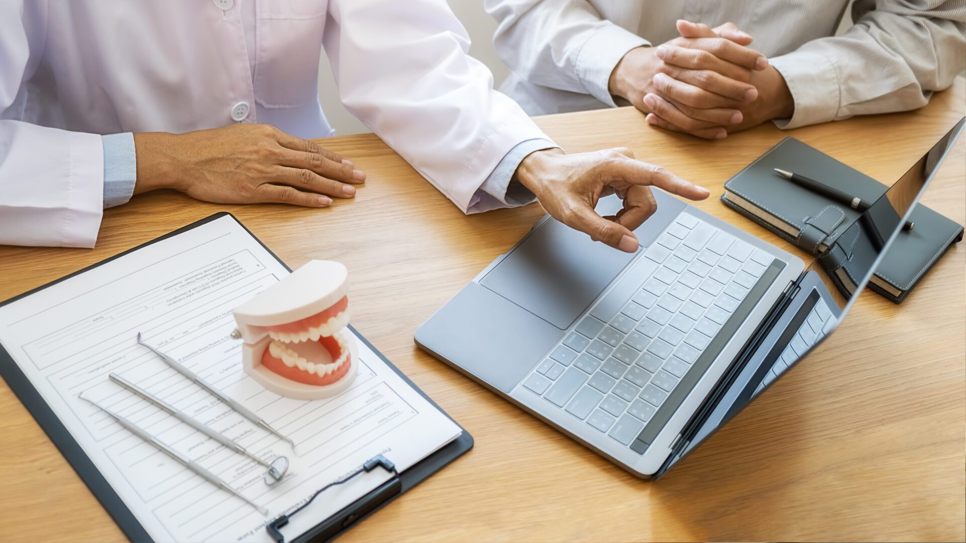 Dentist showing and explaining teeth disease treatment to patient using teeth model denture and explorer mirror tool in dental clinic office